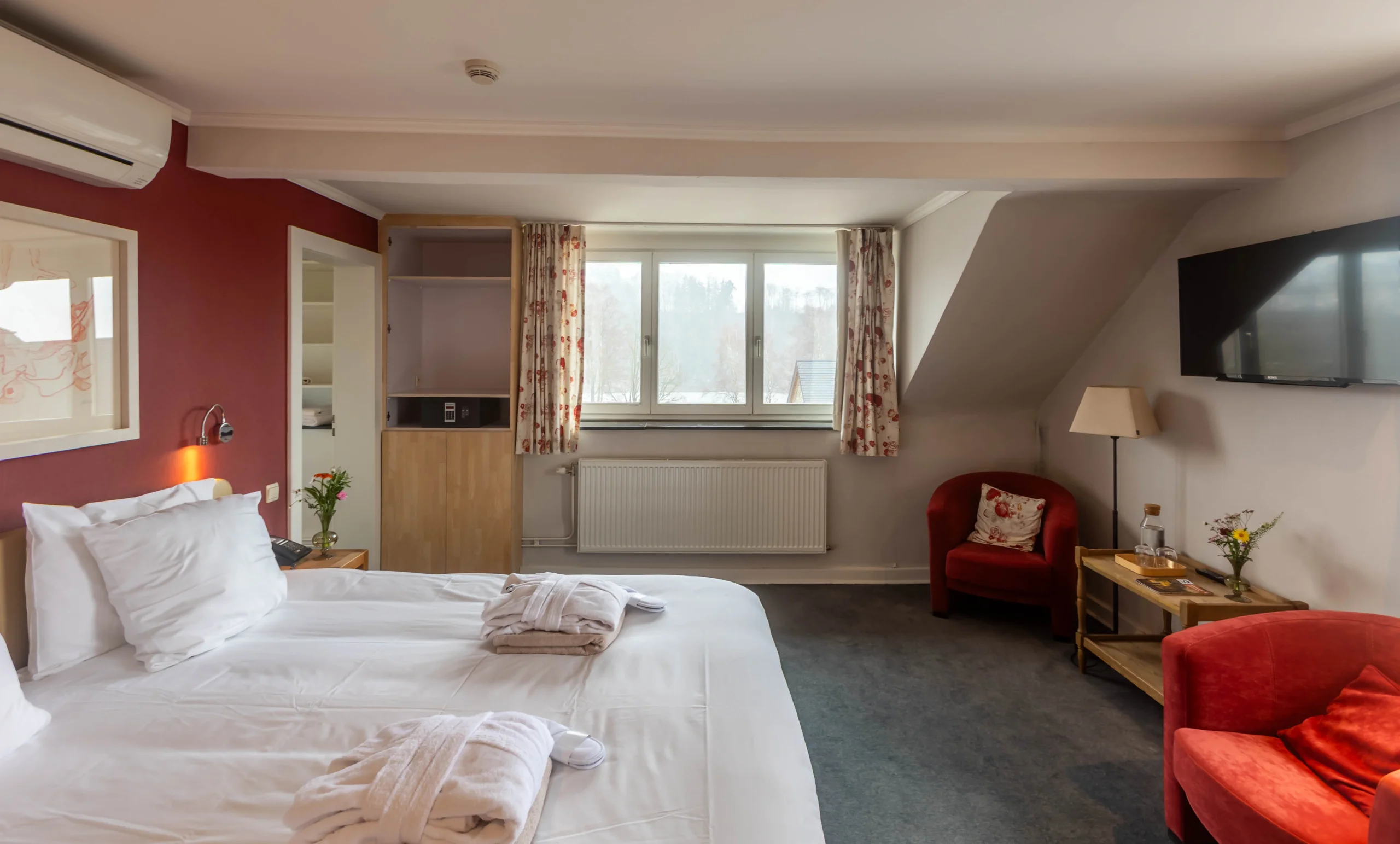 Chambre d'hôtel confortable avec lit et fauteuils rouges.
