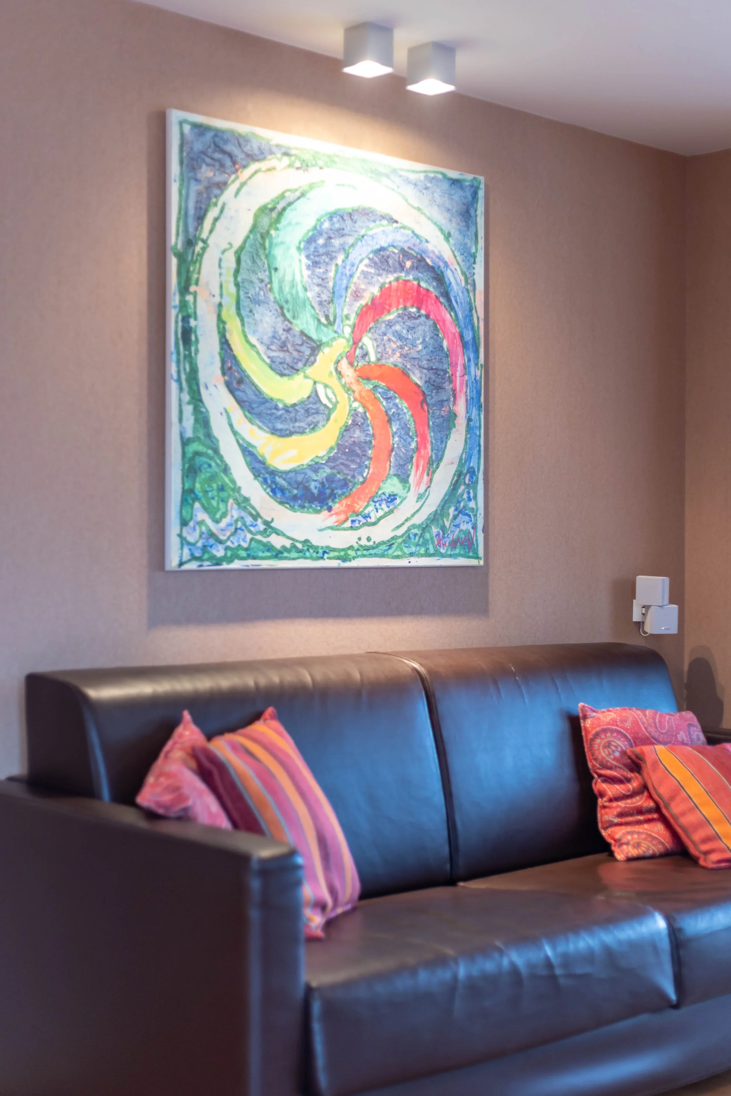 Canapé en cuir avec coussins colorés et tableau.