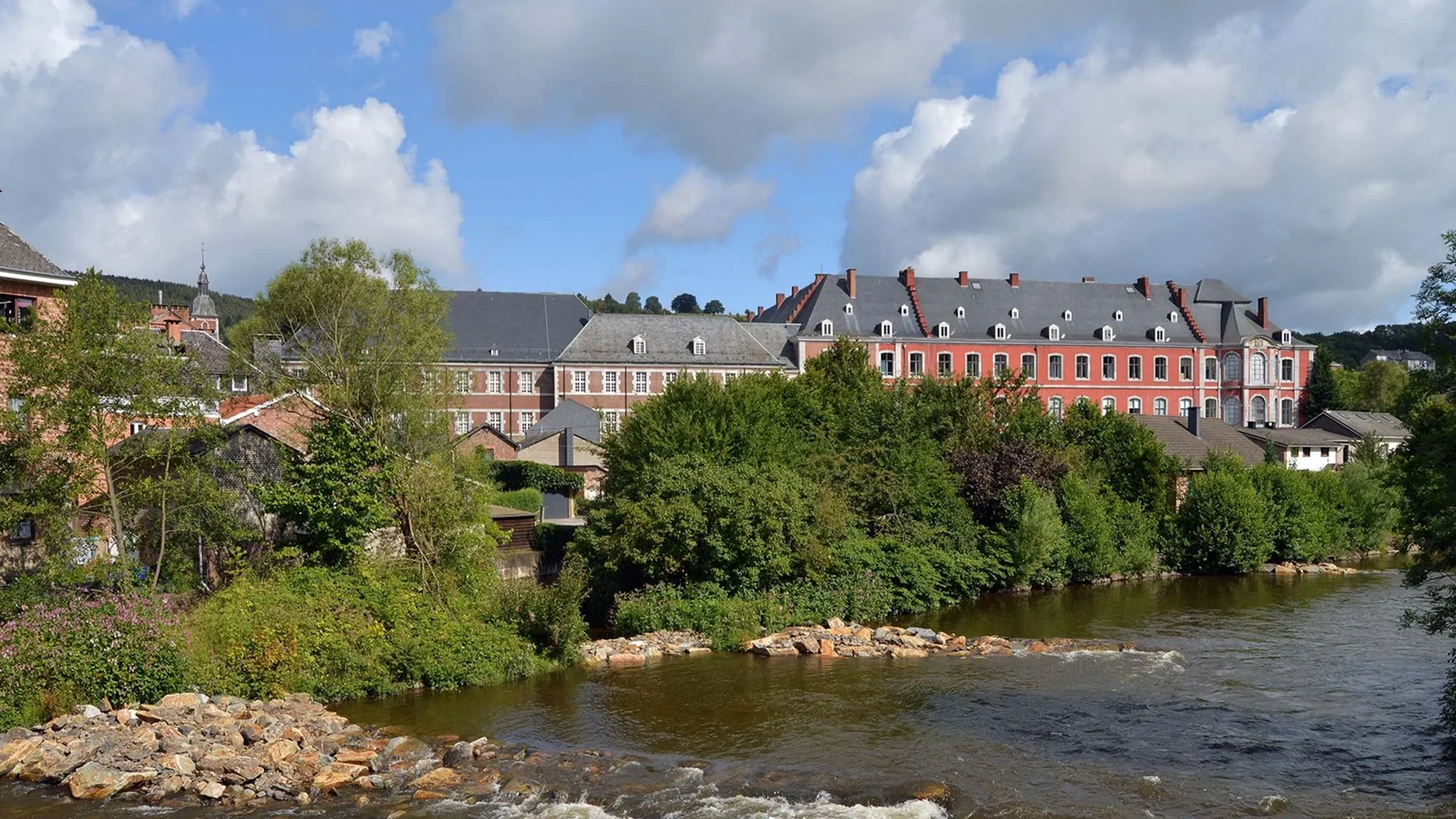 Paysage rivière et bâtiment ancien sous ciel nuageux - Séjour Wellness Belgique - Robert Hôtels