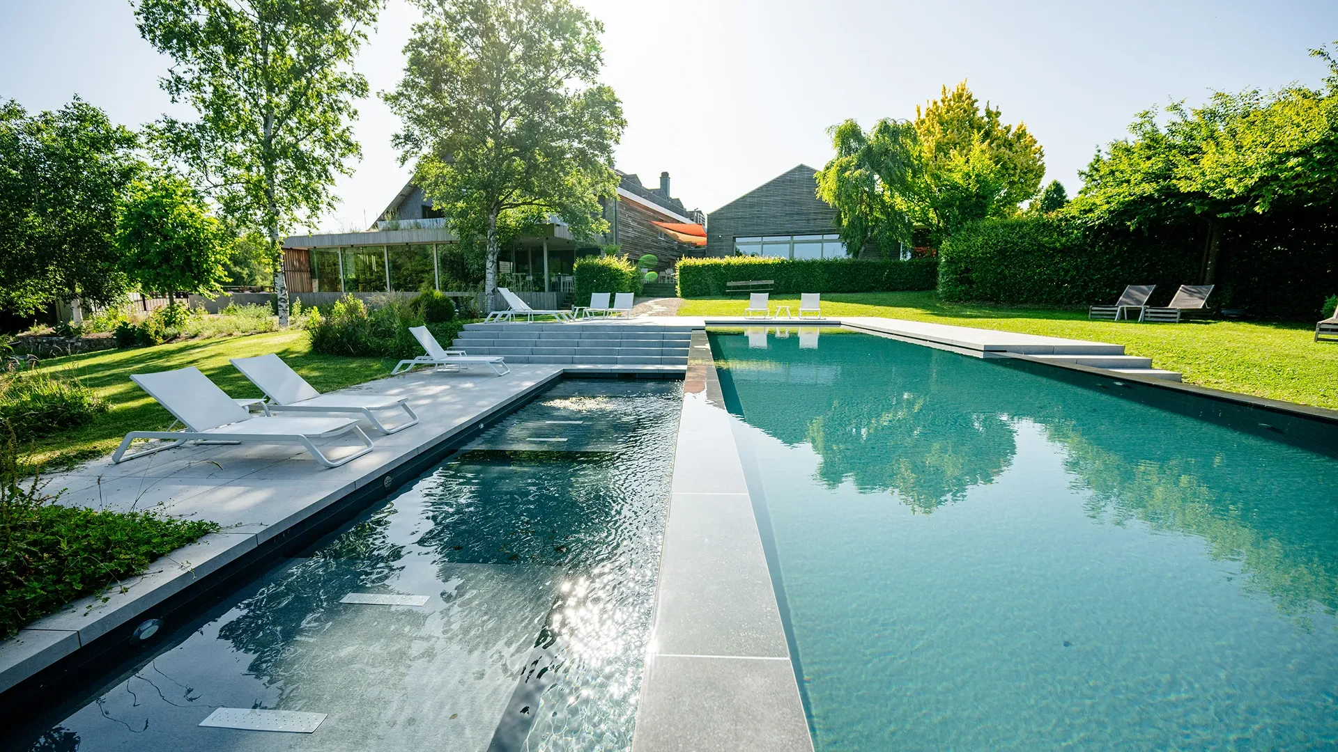Piscine moderne entourée de verdure et chaises longues.