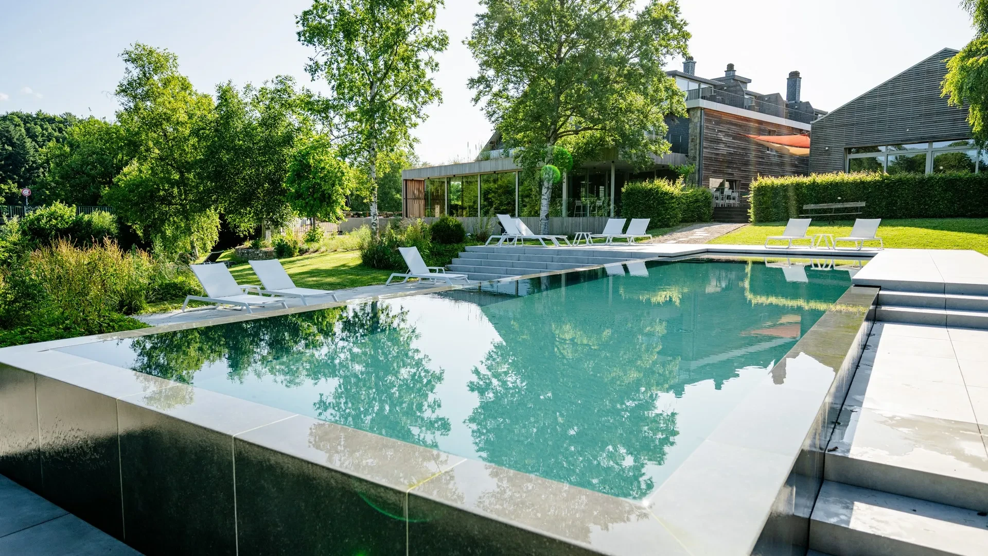 Piscine moderne avec chaises longues et jardin.