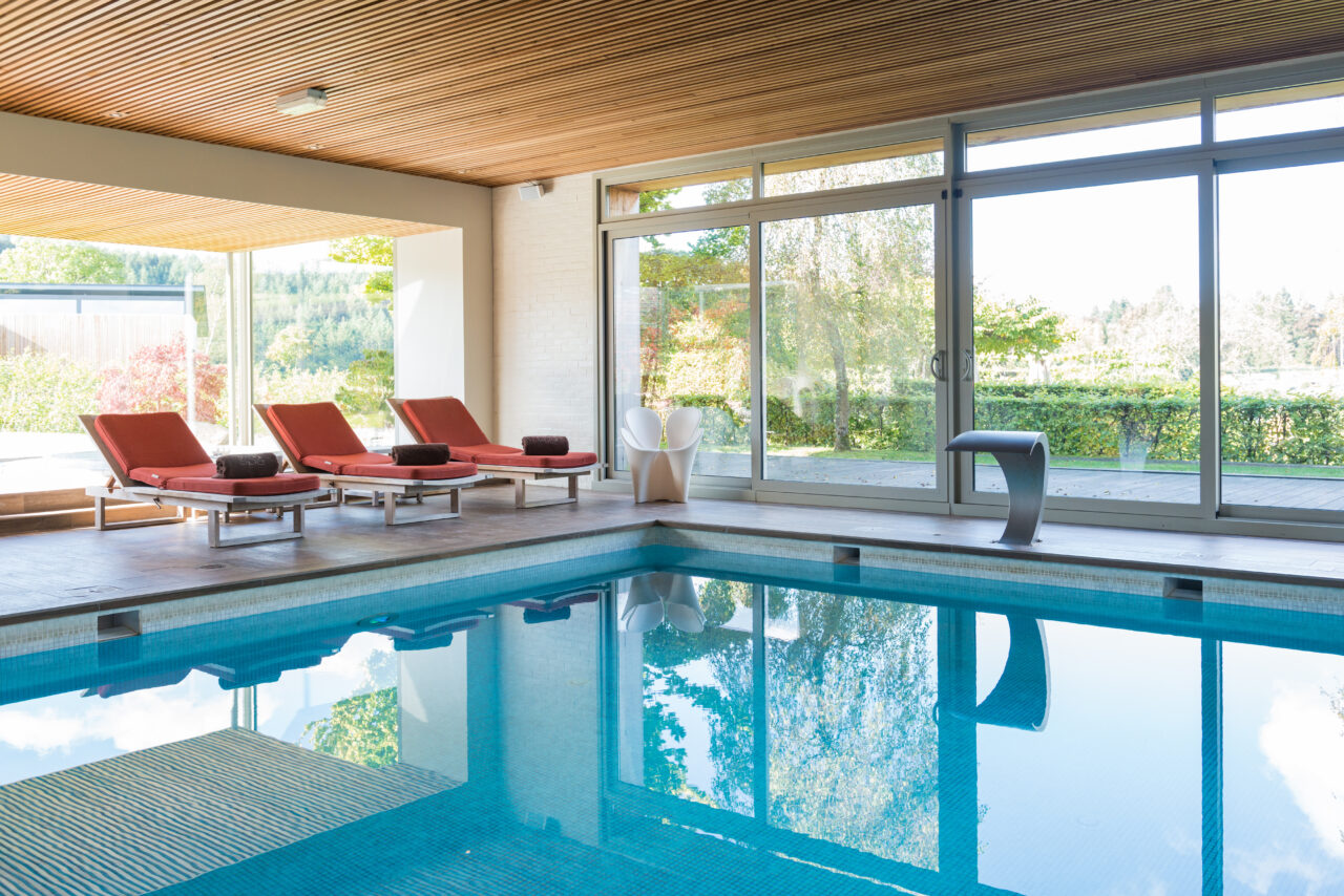 Piscine intérieure avec chaises longues et grandes fenêtres - Hôtel Spa Francorchamps - Robert Hôtels