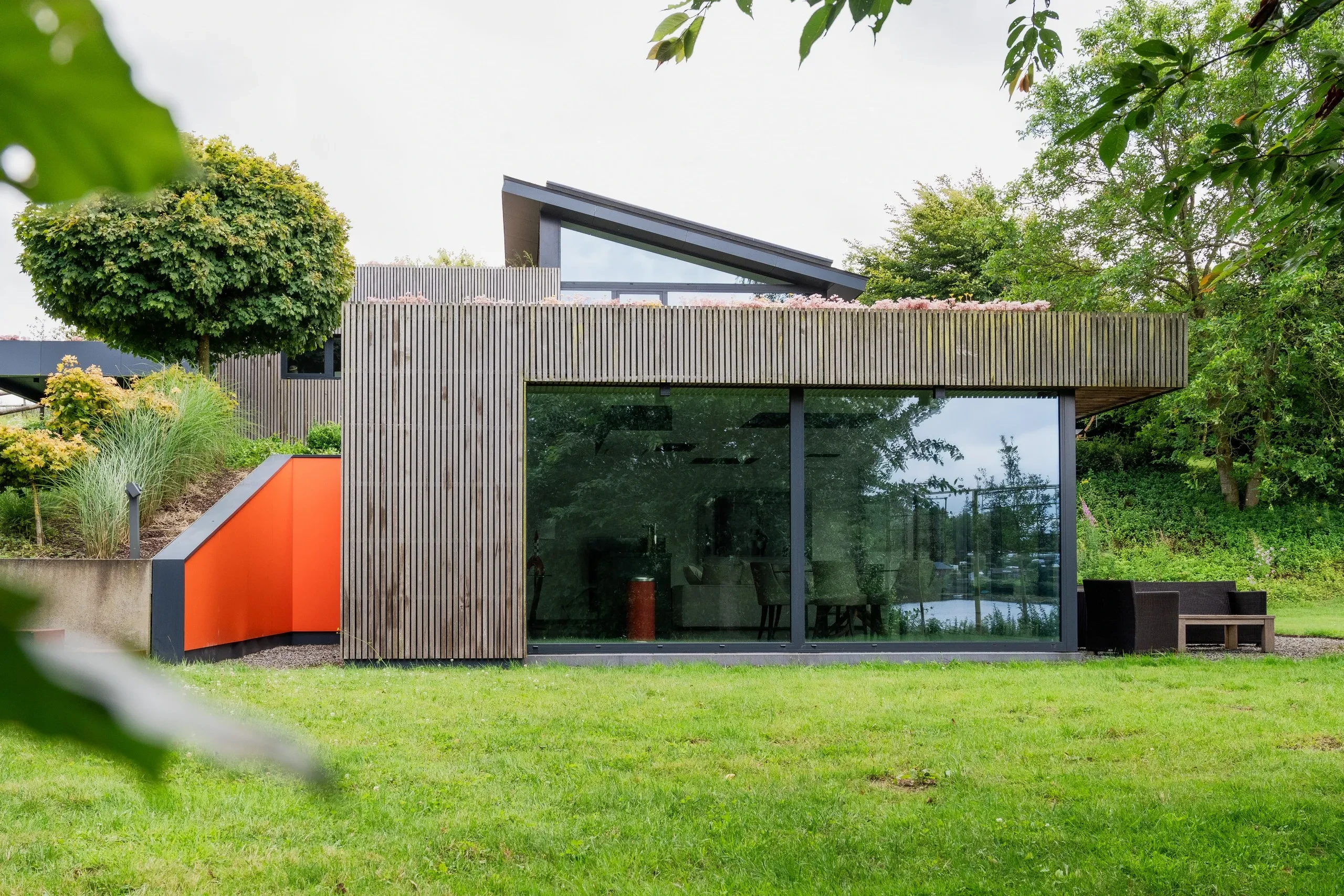 Maison moderne avec grande fenêtre et jardin vert.