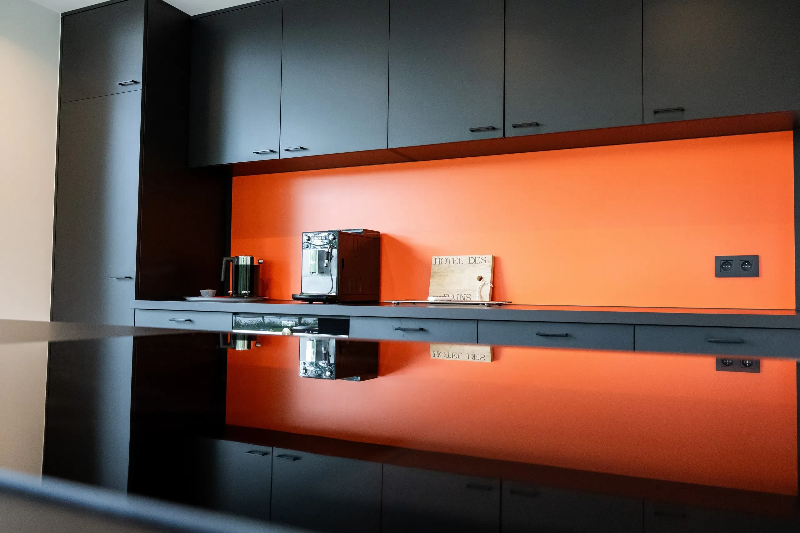 Cuisine moderne avec mur orange et machines à café.